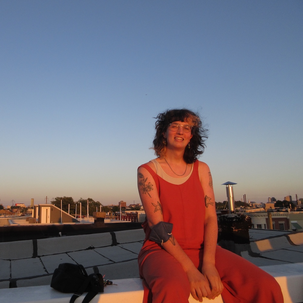A photo of Addie sitting on a roof deck, smiling, at sunset.